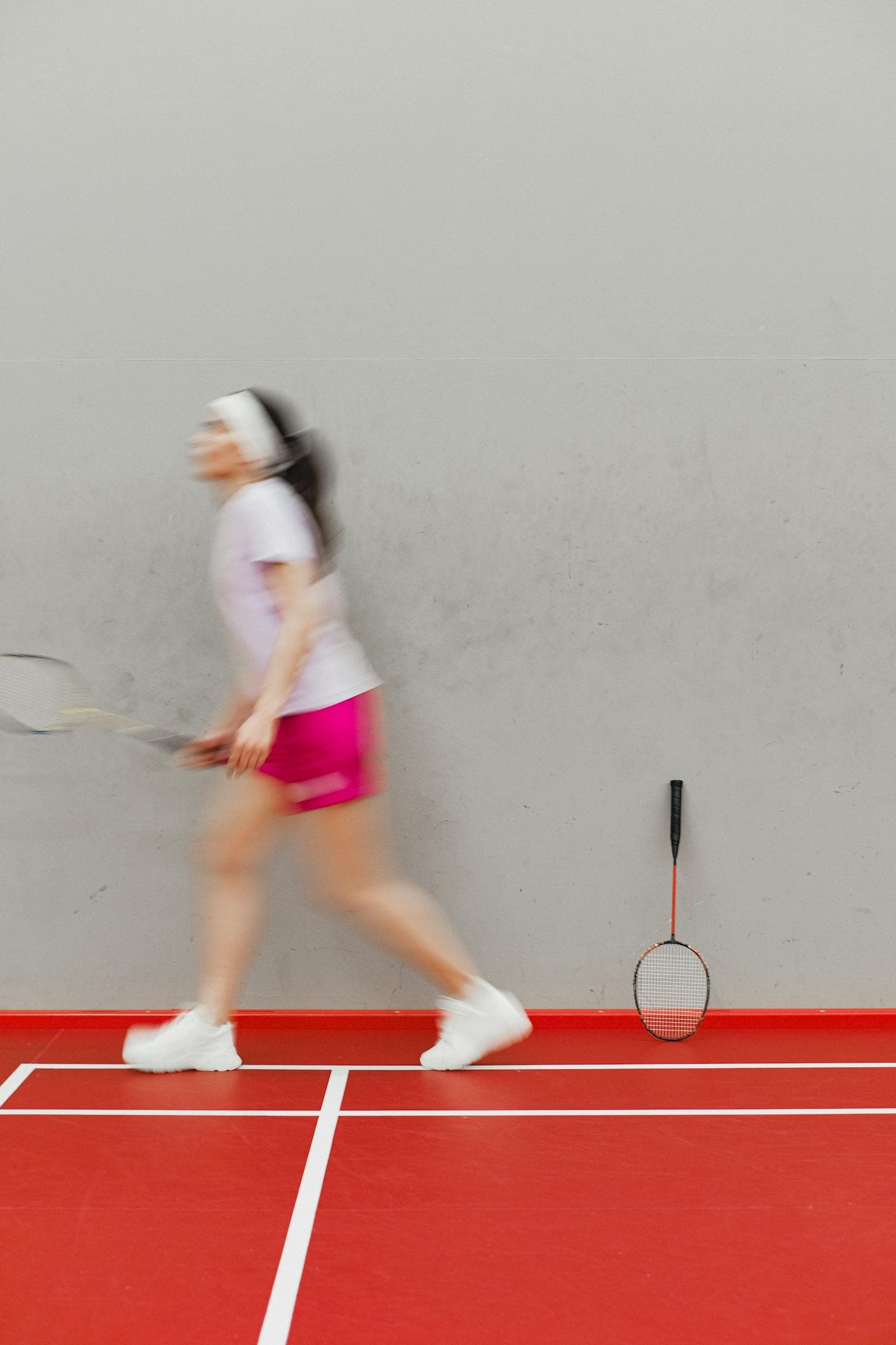 Motion-blurred view of a player mid-swing on a red indoor badminton court, racket in motion