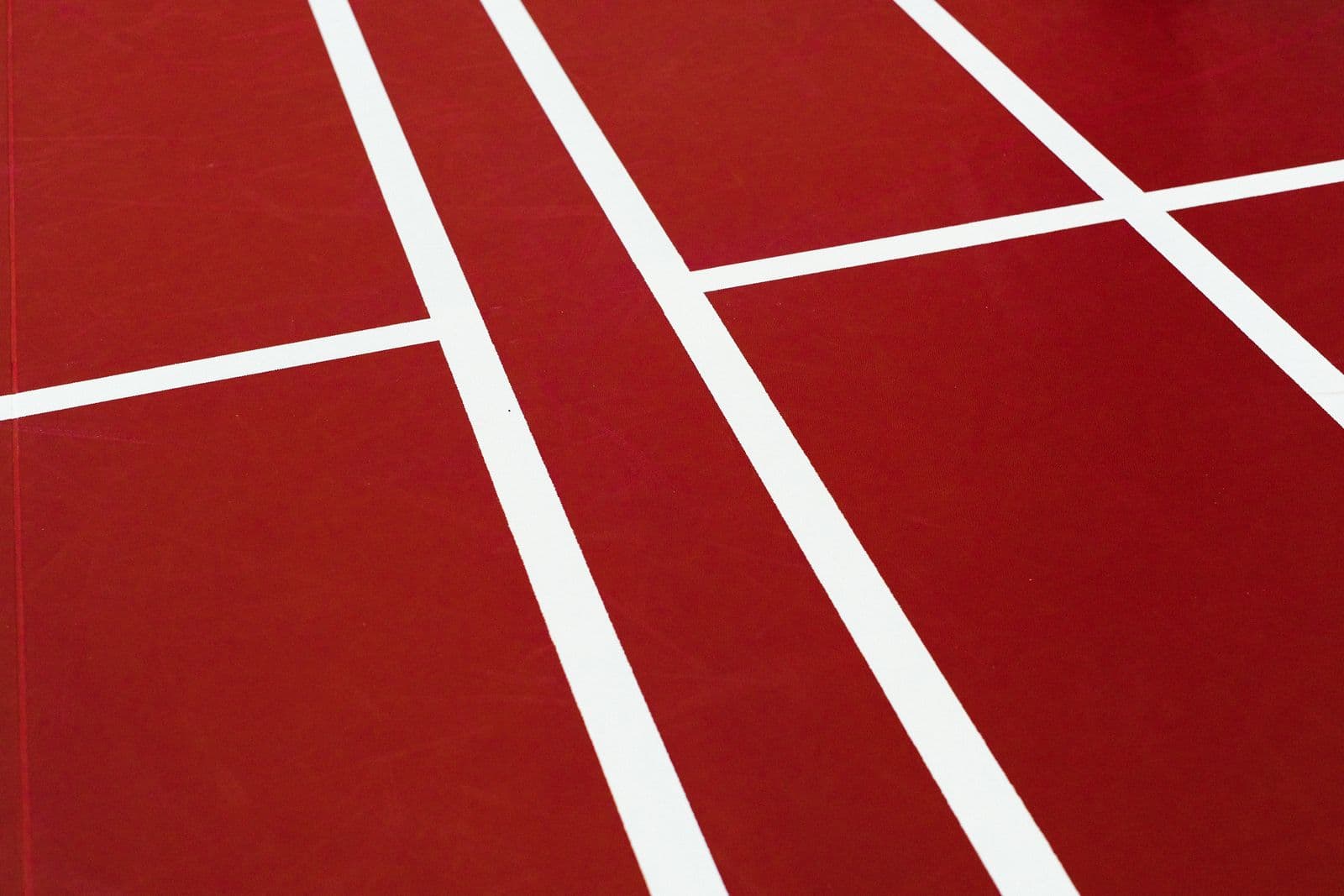 Close-up of white court lines intersecting on a red indoor badminton court surface