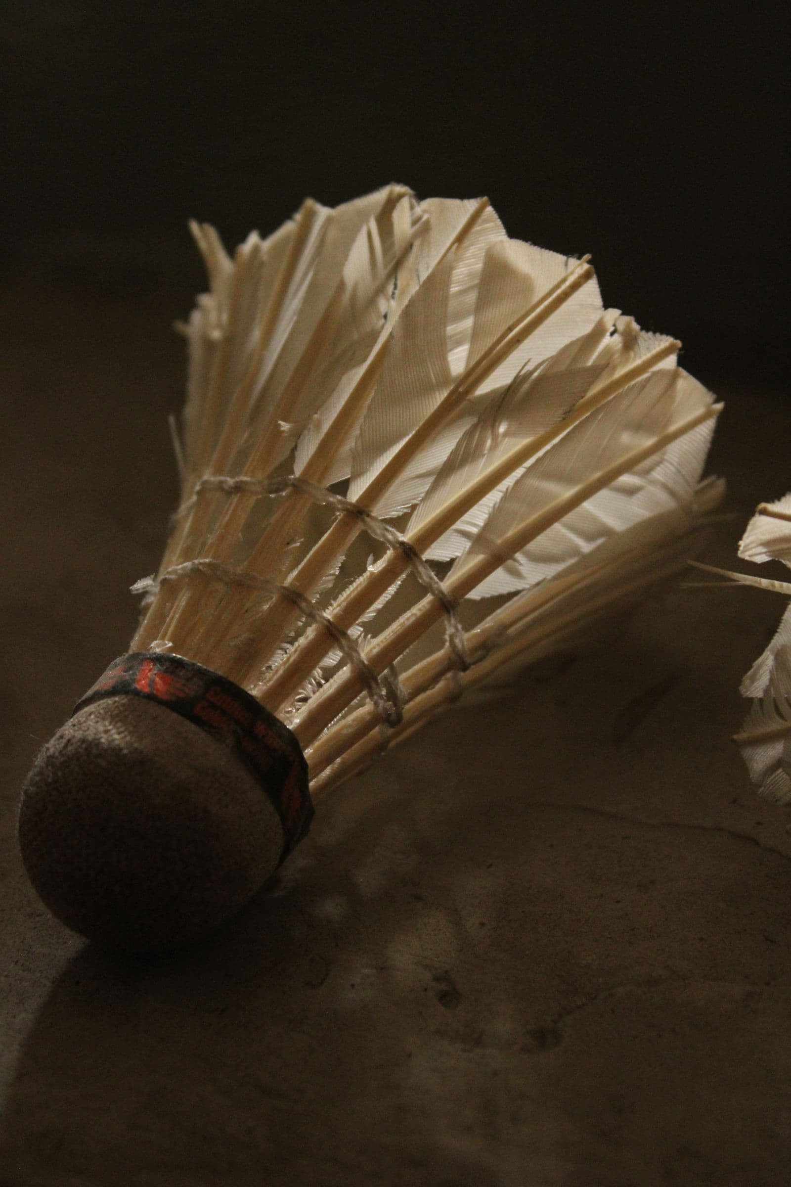 Close-up of a badminton shuttlecock in dramatic warm side-lighting against a dark textured surface