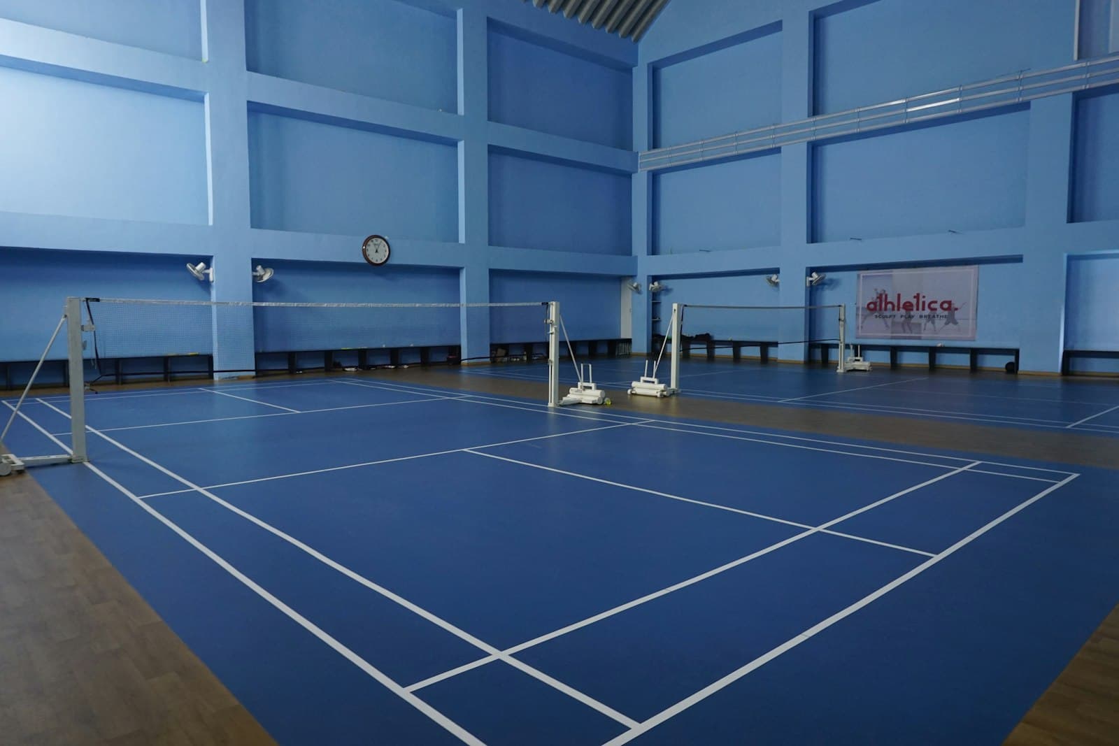 Empty indoor badminton courts with blue flooring and painted court lines