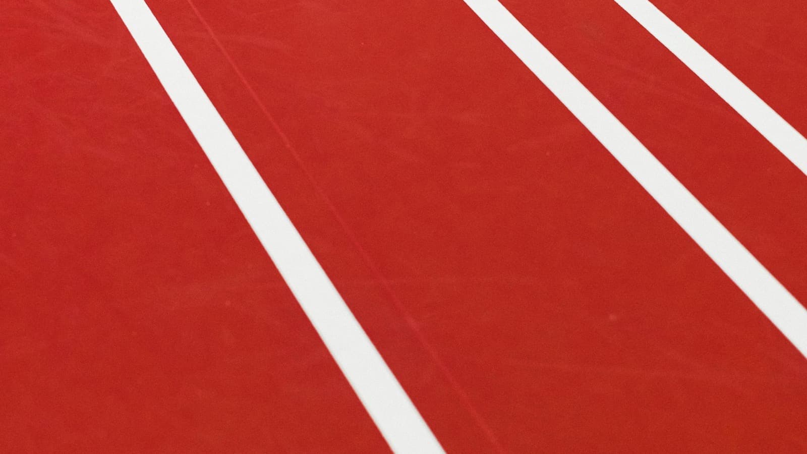 A single white shuttlecock lying on a red indoor badminton court between white boundary lines