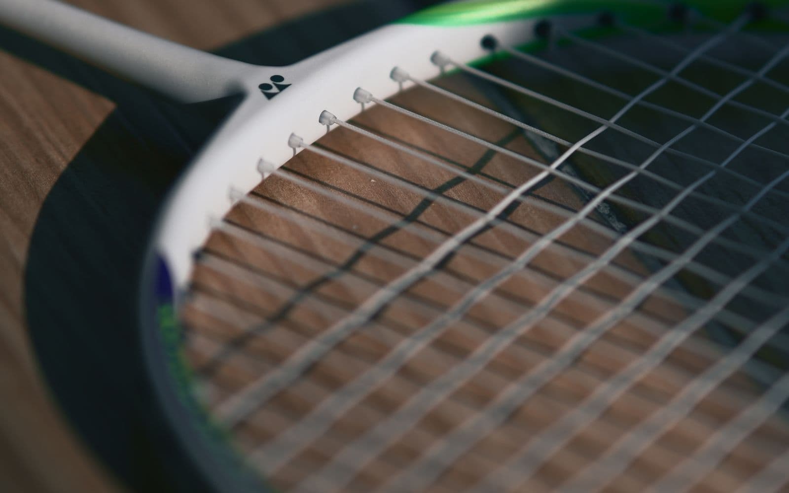 Close-up of a badminton racket's strings resting on a wooden court floor