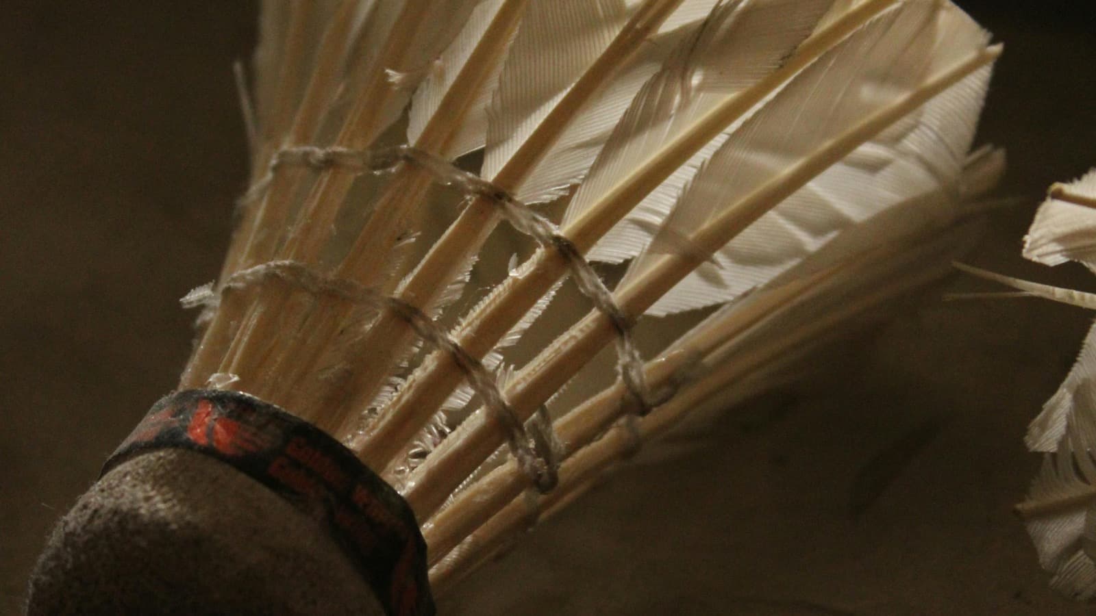 Close-up of a single white shuttlecock against a dark background with dramatic high-contrast lighting