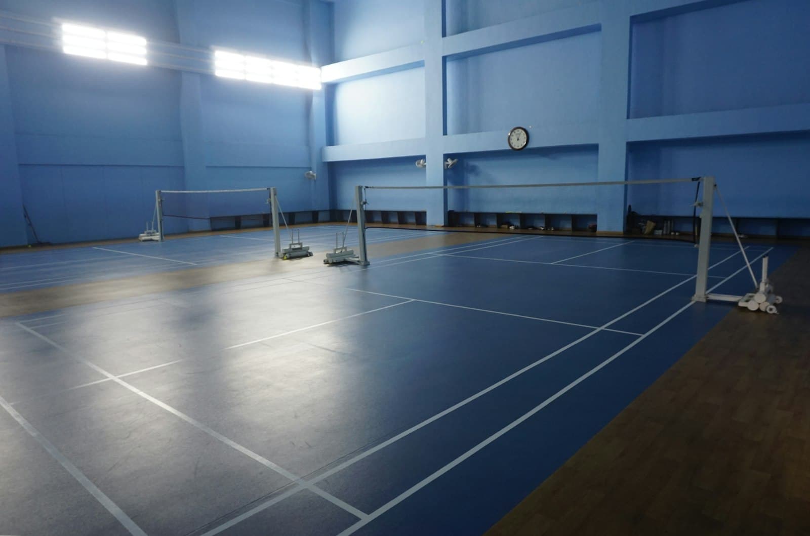 Empty high-ceilinged indoor badminton hall with blue walls and painted court lines