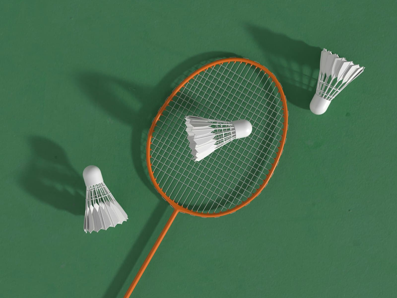 An orange badminton racket and two white shuttlecocks on a green court surface, top-down composition