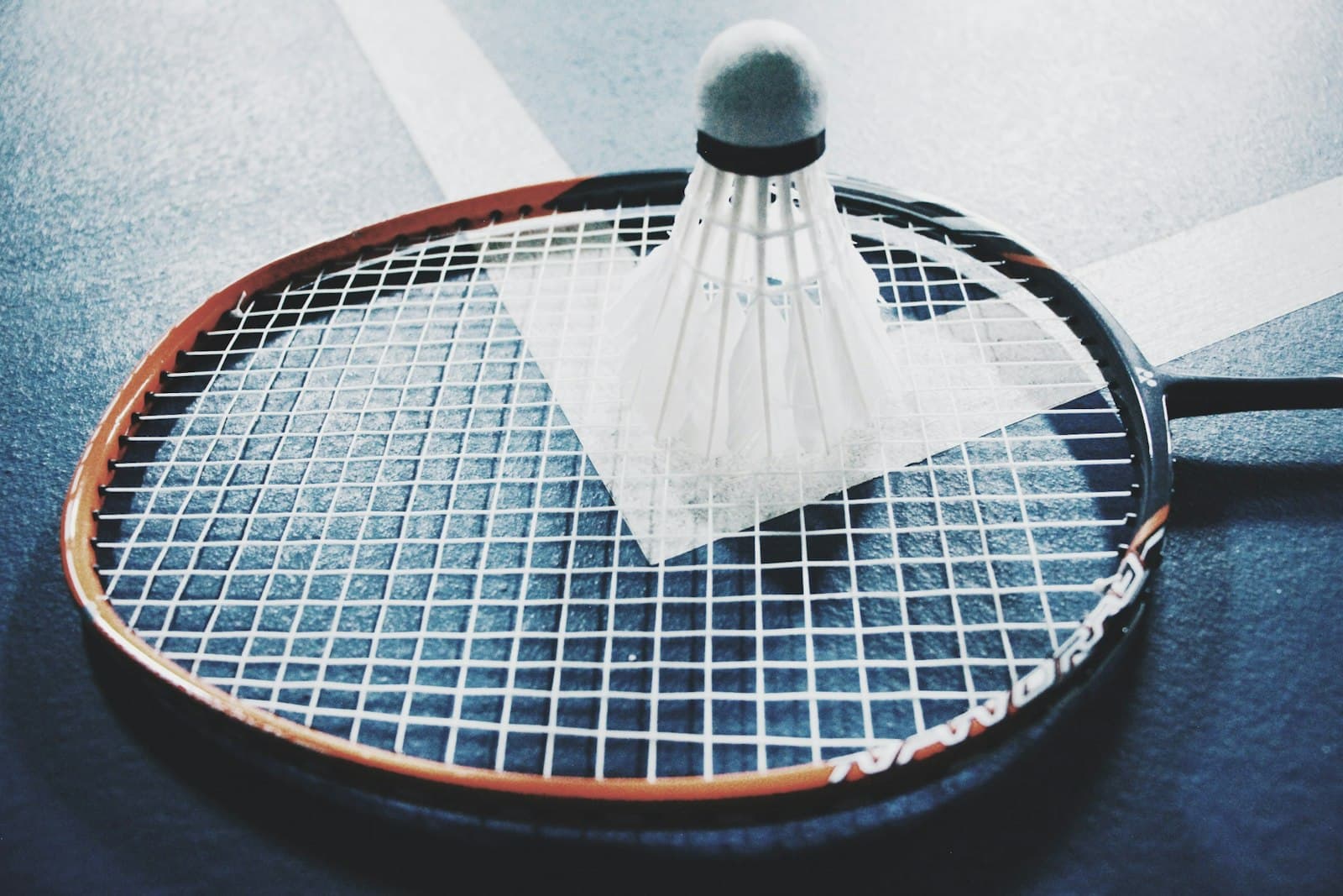 A white shuttlecock resting on a brown and black badminton racket placed on an indoor wooden court floor